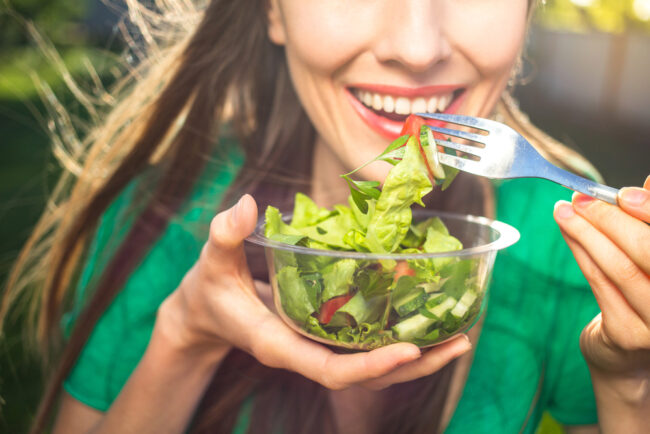 woman smiling holding a salad for healthy teeth